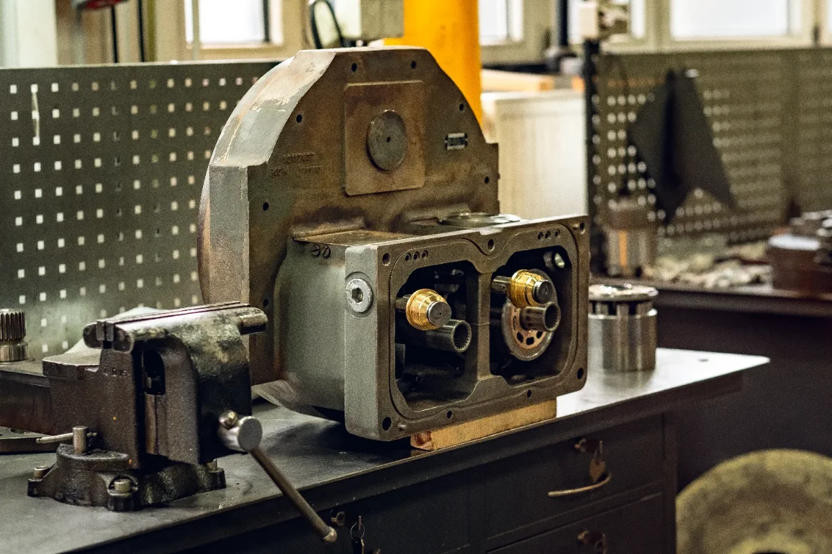 Opened hydraulic pump housing with visible internal parts, clamped in a vice on the workbench