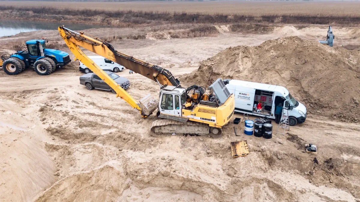 Liebherr long-reach crawler excavator being serviced in a gravel pit next to a WIBAKO service van and oil drums