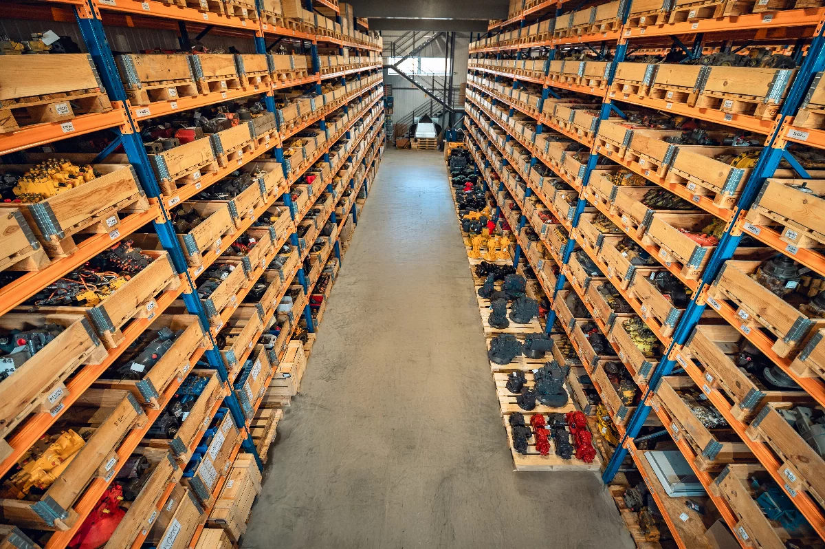 Parts warehouse with racks full of crates holding hydraulic pumps and construction machine components