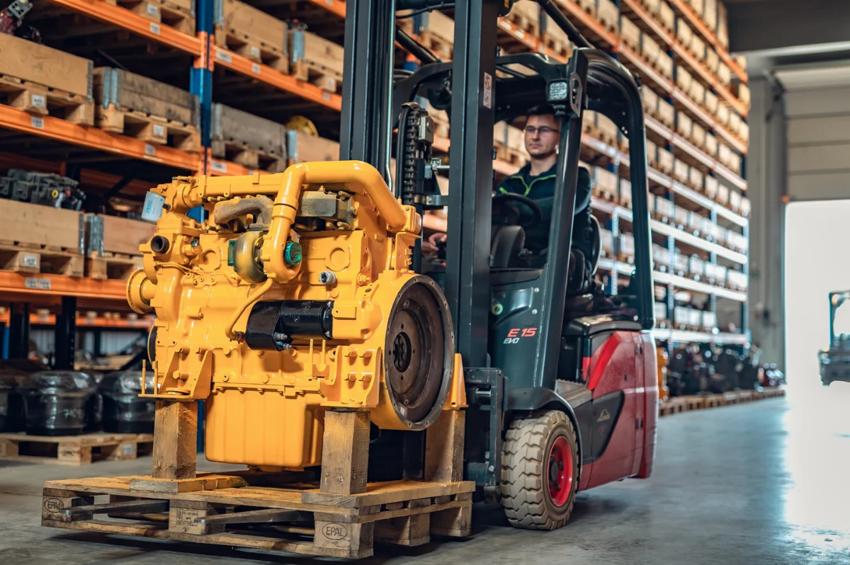 Forklift carrying a remanufactured yellow diesel engine on a pallet in a warehouse hall