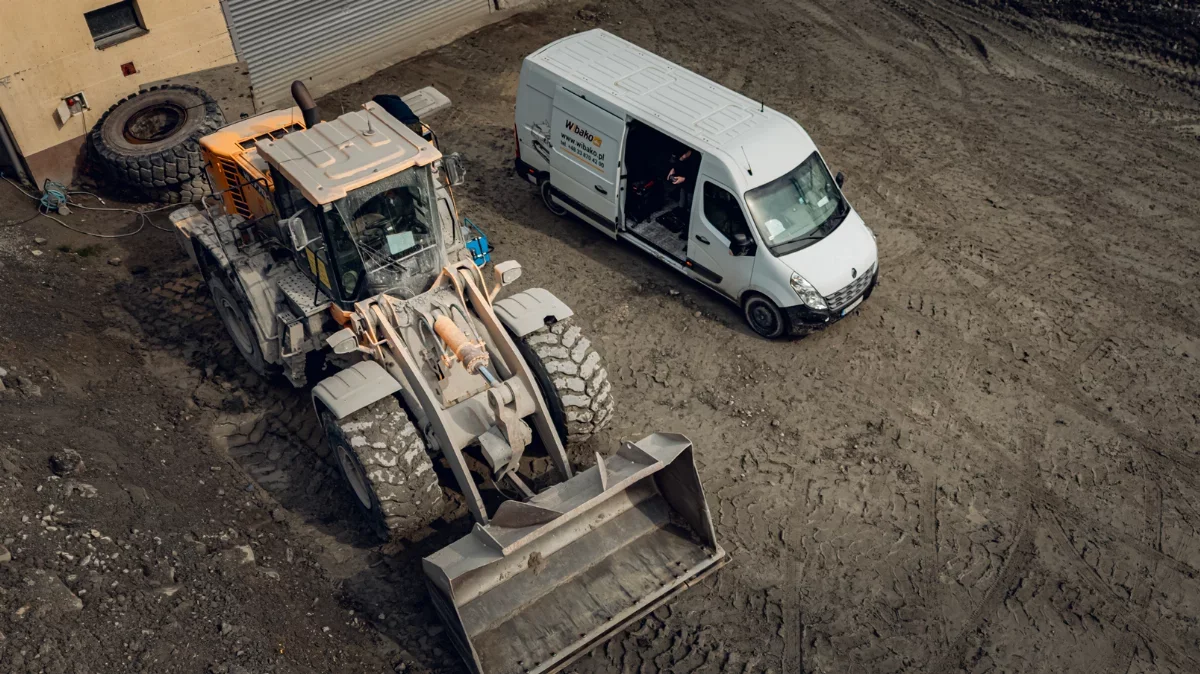 Wheel loader and WIBAKO service van with open doors in a yard, aerial view