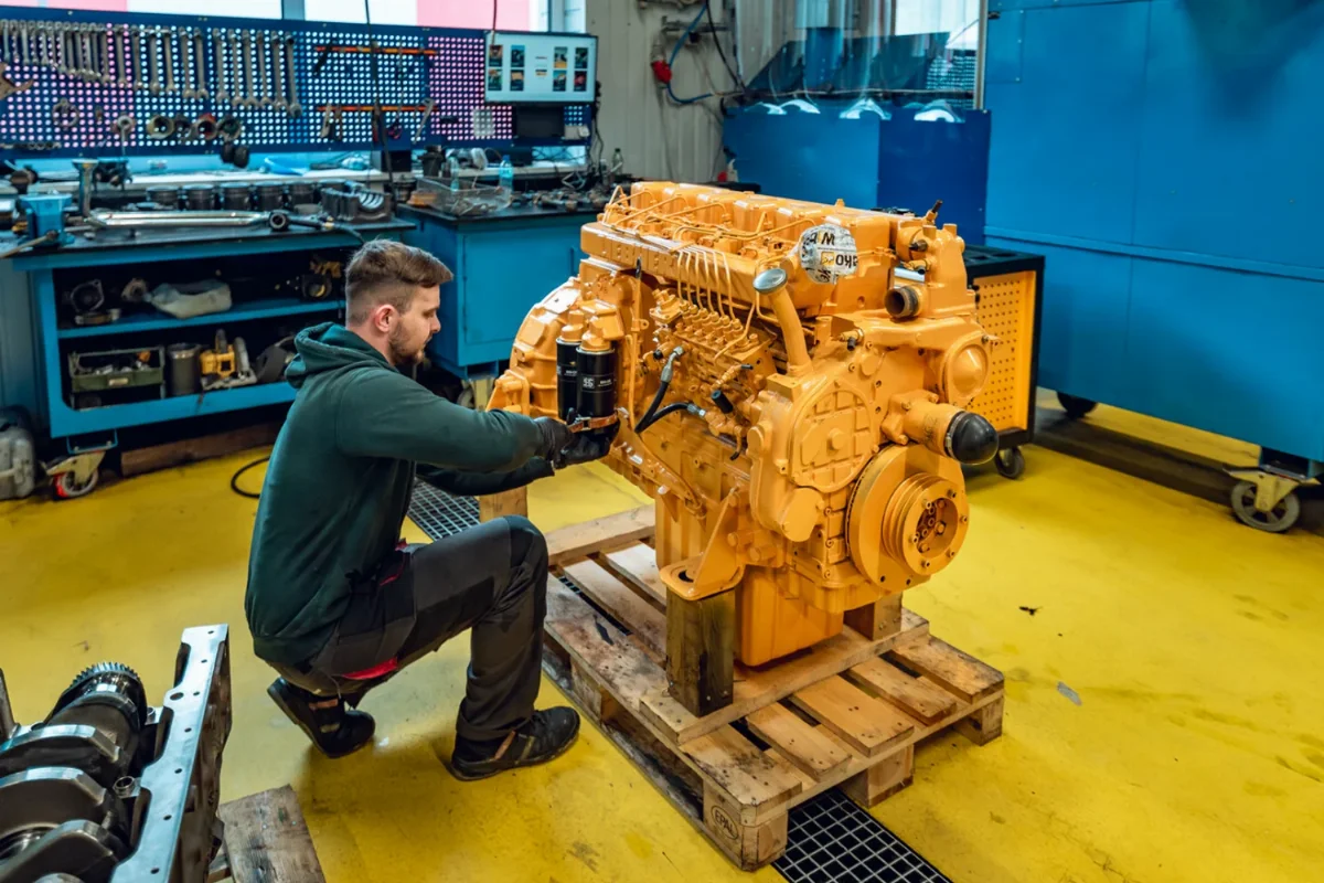 Mechanic fitting filters to an overhauled, yellow-painted diesel engine on a pallet