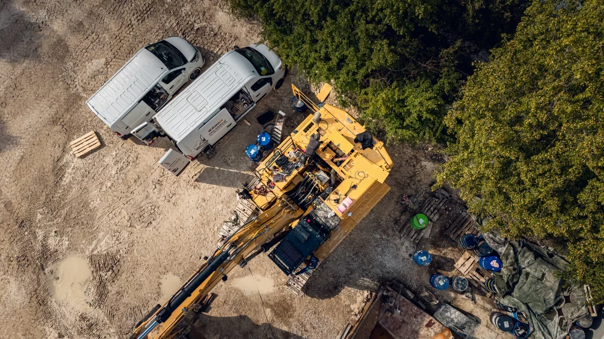 Drone view of a crawler excavator being serviced in the field next to two white service vans