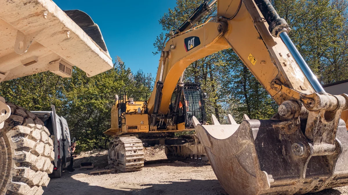 CAT crawler excavator with bucket in the foreground and a service van in the yard