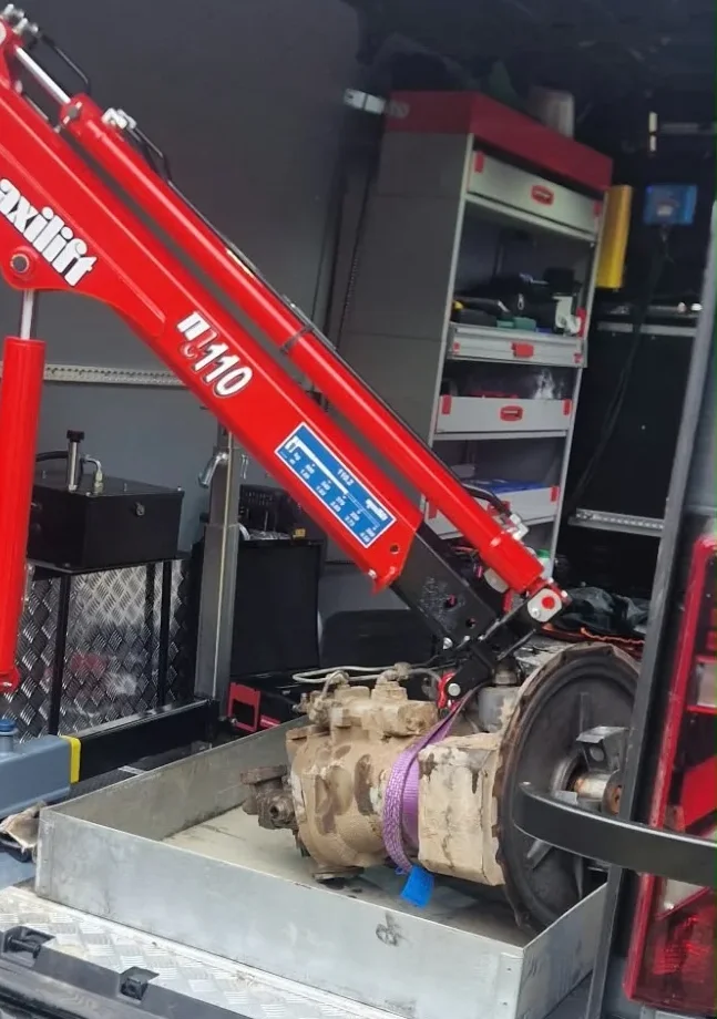Removed excavator hydraulic pump in a drip tray in the service van under the arm of a red crane
