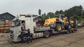 Liebherr 566 wheel loader on a low-bed trailer pulled by a Volvo truck at the company yard