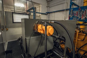 Yellow hydraulic pump connected with hoses to a test bench in a workshop hall
