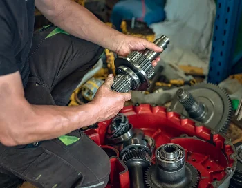 Mechanic holding a gear shaft above an open transmission housing of a construction machine