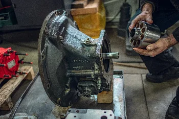 Mechanic holding a hydraulic pump cylinder block next to a disassembled axial piston pump housing in a workshop
