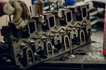Diesel engine cylinder head on a workbench during reconditioning, with a removed valve standing beside it