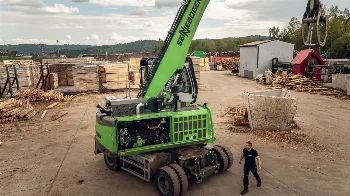 Wheeled Sennebogen material handler with exposed engine on a sawmill yard with timber stacks