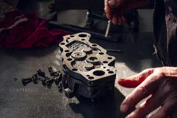 Mechanic assembling a hydraulic pump housing on a workbench with mounting bolts laid out beside it