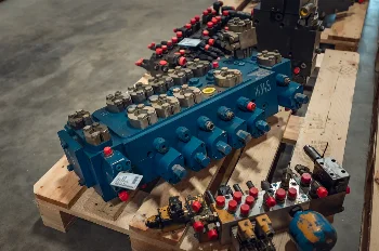 Blue multi-section hydraulic control valve with capped ports and a valve block on a pallet in the warehouse