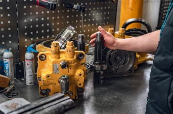 Mechanic holding a splined shaft next to a disassembled CAT swing motor on a workshop bench