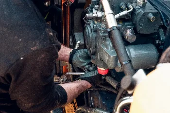 Mechanic in gloves using a wrench on a hydraulic pump mounted in a construction machine