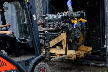 Forklift moving a V8 engine mounted on a wooden pallet into a container