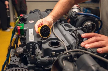 Mechanic removing the yellow oil filler cap from the valve cover of a diesel engine next to the turbocharger