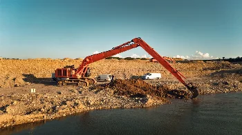 Orange crawler excavator with long-reach boom digging material from water in a gravel pit