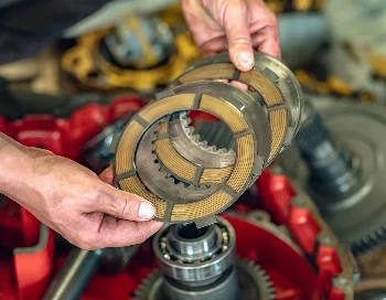 Clutch friction discs with lining held in hands above a disassembled transmission