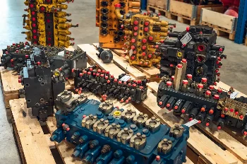 Collection of yellow, black and blue hydraulic control valves on pallets in a warehouse hall