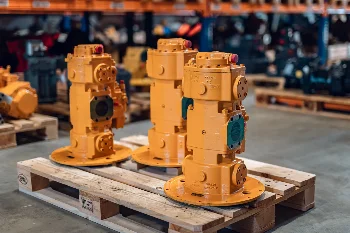 Three remanufactured hydraulic pumps in yellow paint standing on a pallet in a parts warehouse