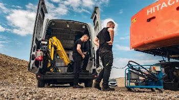 Mobile hydraulic service van with crane and oil filtration unit next to a Hitachi excavator at a gravel pit