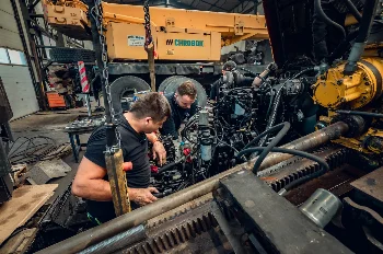 Mechanics working on a diesel engine in the open engine bay of a CHROBOK mobile crane in a service hall
