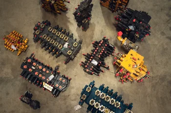 Top view of various construction machine hydraulic control valves laid out on a concrete floor