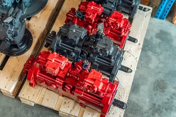 Red and dark grey tandem hydraulic piston pumps laid out on a wooden pallet in a warehouse