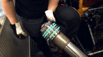 Mechanic in gloves holding a hydraulic cylinder piston rod fitted with new green sealing and guide rings